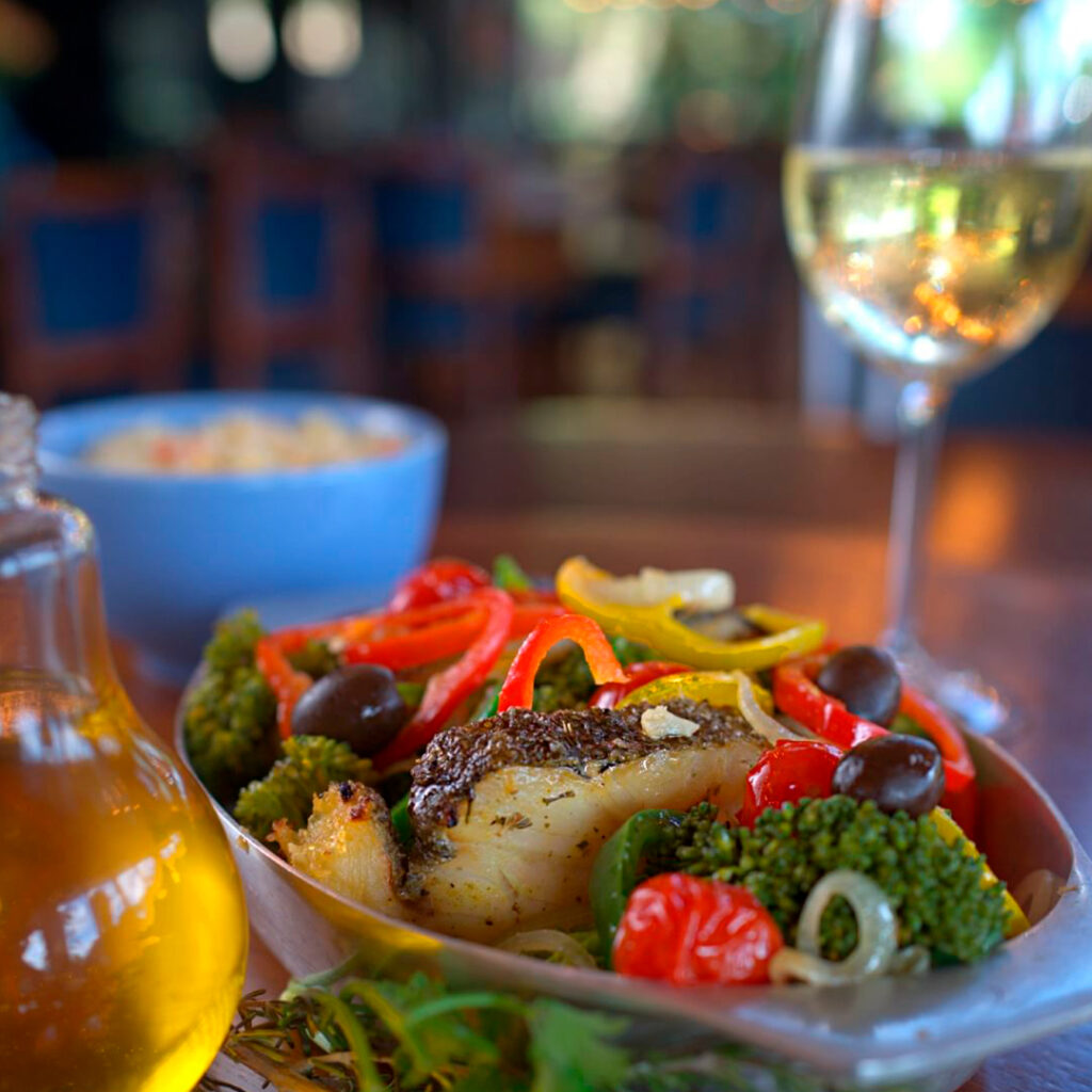 Travessa de bacalhau com legume e taças de vinho sobre uma mesa