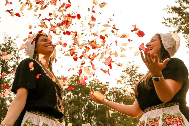 Duas garotas com roupas típicas holandesas jogando pétalas para o alto na Expoflora enquanto sorriem